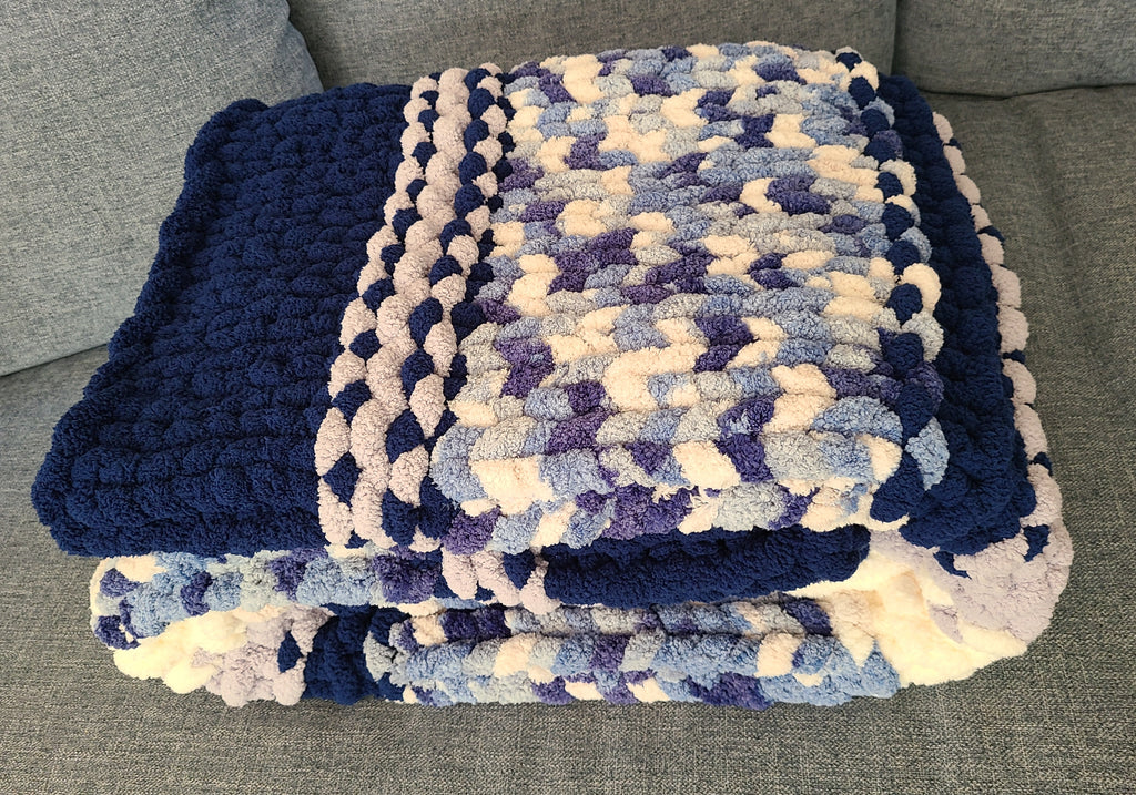Winter Solstice — deep navy, light gray, and cream — folded on a gray sofa showing the navy border