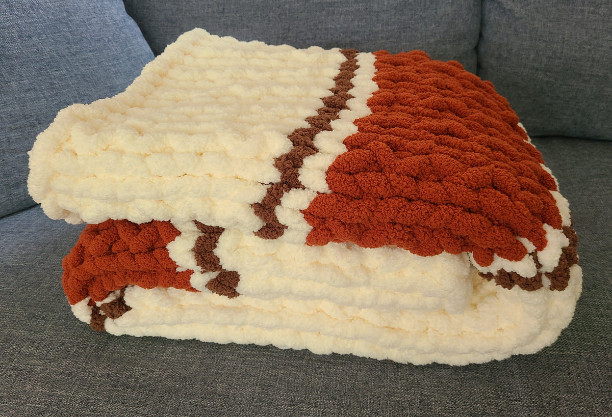 Autumn Ember — copper, coffee brown, and vintage white — folded on a blue sofa showing the knit depth