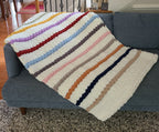 Timeless Eras — multicolour raised stripes on cream — draped over a gray sofa showing the stripe sequence