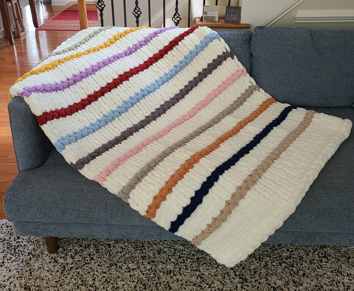 Timeless Eras — multicolour raised stripes on cream — draped over a gray sofa showing the stripe sequence