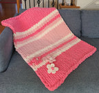 Hibiscus Bloom baby blanket — bright pink gradient — draped over the arm of a gray sofa