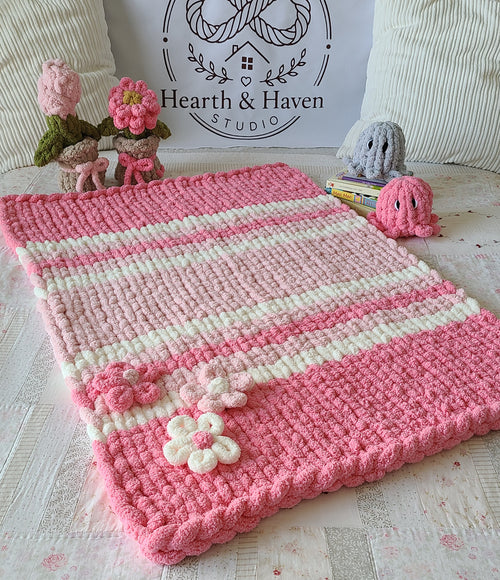 Hibiscus Bloom baby blanket — bright pink gradient — spread on a bed with crochet flowers and toys