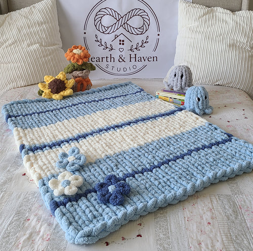 Bluebell Breeze baby blanket — sky blue and cream — spread on a bed with crochet flowers and toys