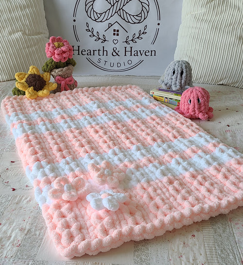 Blushing Mist baby blanket — white and soft pink — spread on a bed with crochet flowers and toys