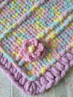 Lullaby Blossom baby blanket — pastel plaid with a lilac border — close-up of the crochet flower and chunky border