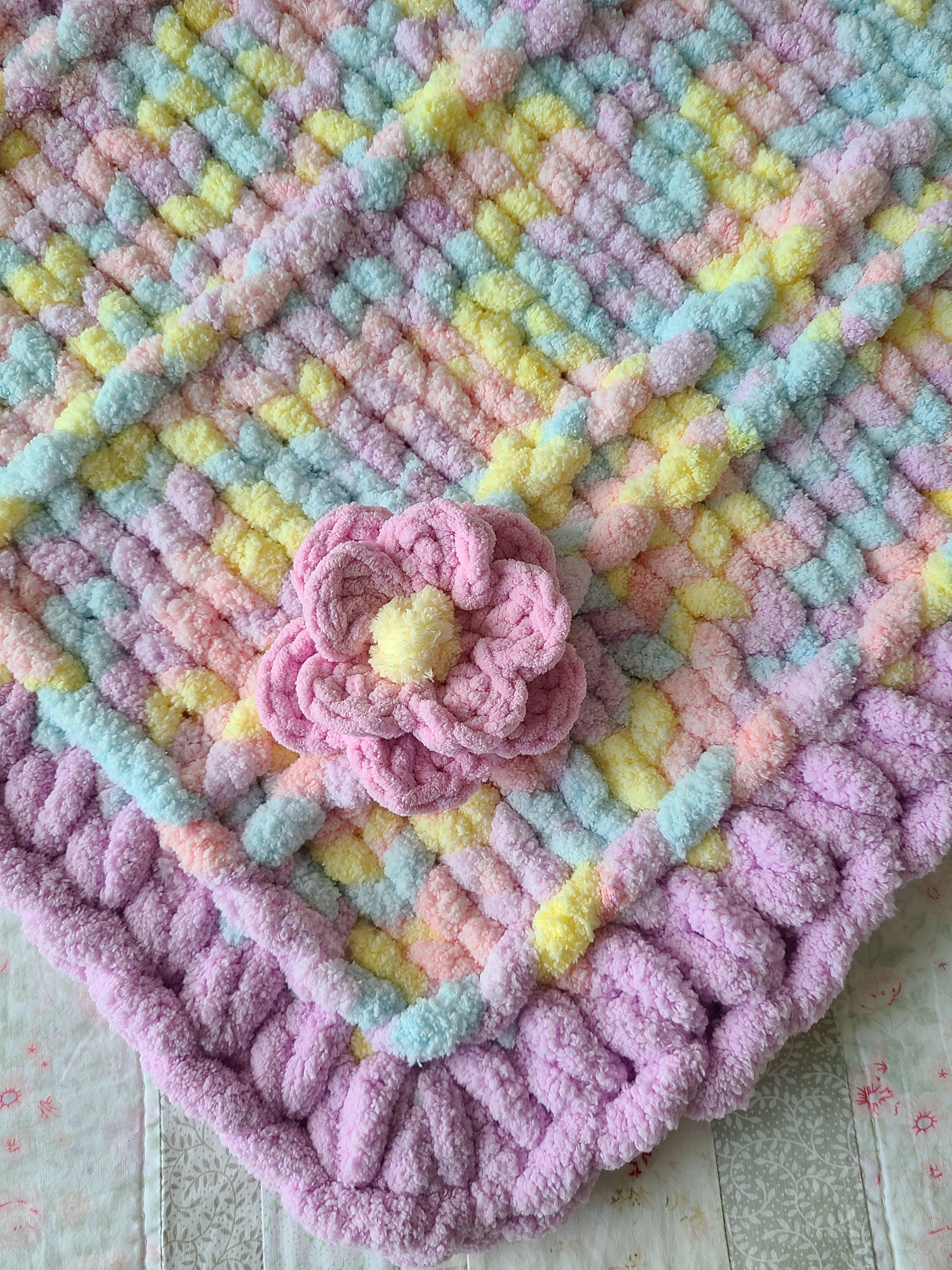 Lullaby Blossom baby blanket — pastel plaid with a lilac border — close-up of the crochet flower and chunky border