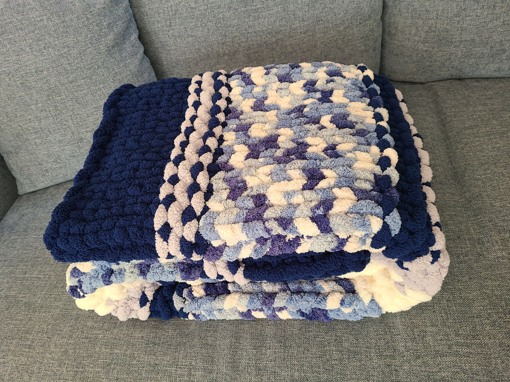 Winter Solstice — deep navy, light gray, and cream — folded on a gray sofa showing the navy border