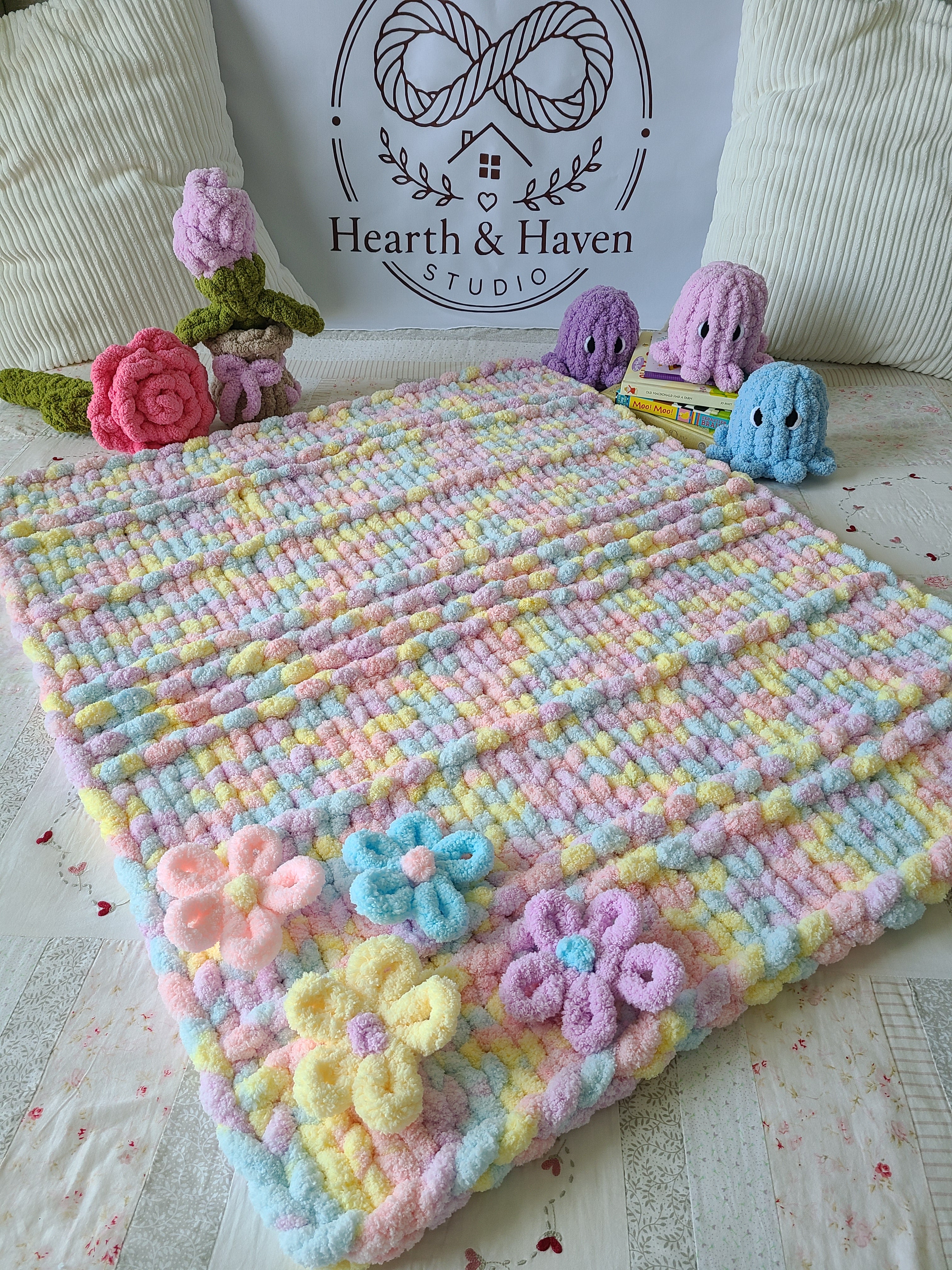 Wildflower Whisper baby blanket — pastel macaron tones — spread on a bed with crochet flowers and toys