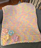 Wildflower Whisper baby blanket — pastel macaron tones — draped over a gray armchair