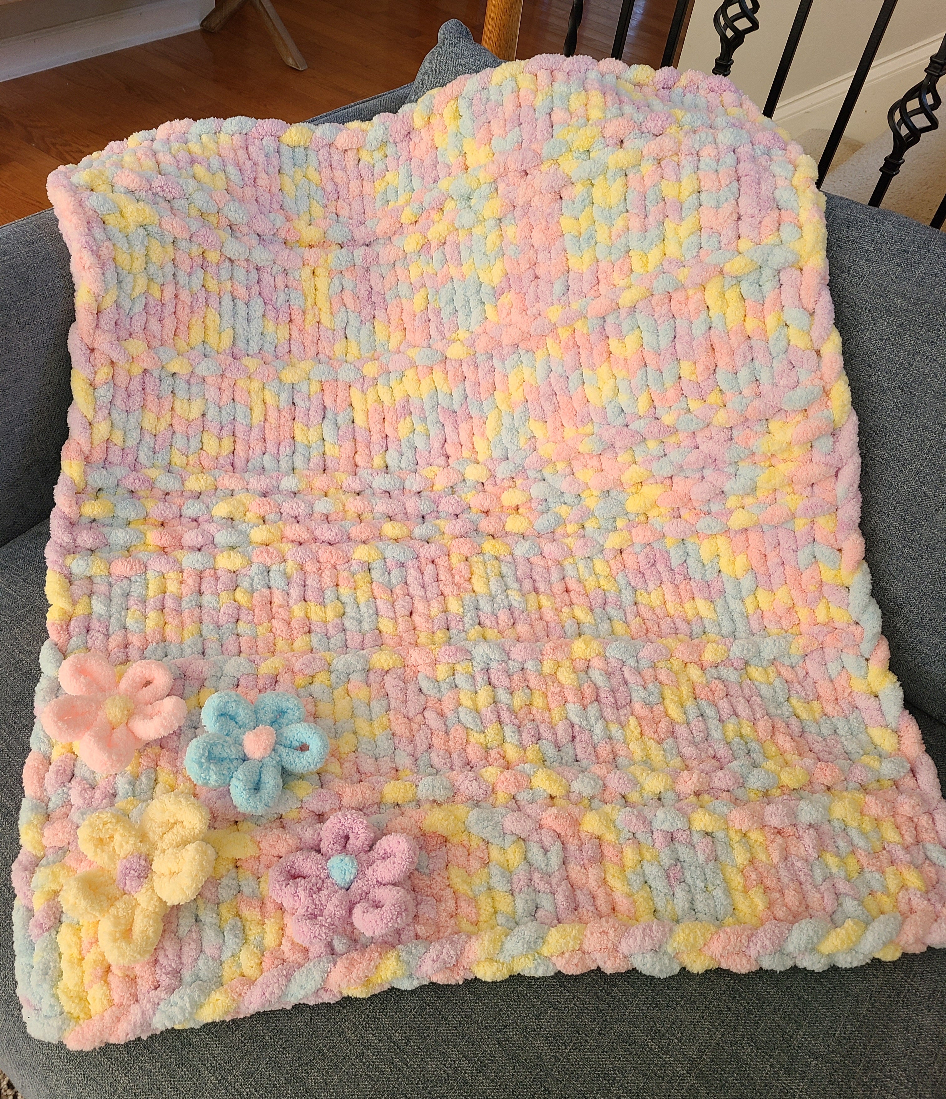 Wildflower Whisper baby blanket — pastel macaron tones — draped over a gray armchair