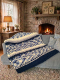 Winter Solstice — deep navy, light gray, and cream — draped over a sofa beside a lit stone fireplace