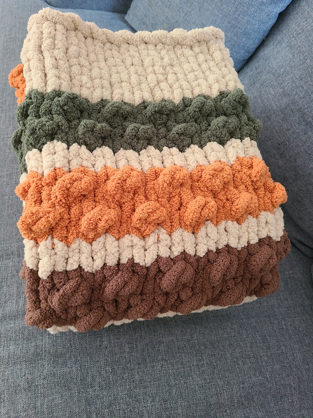 Woodland Ridge — olive, butterscotch, and taupe on oatmeal — folded on a sofa showing the stacked bobble bands