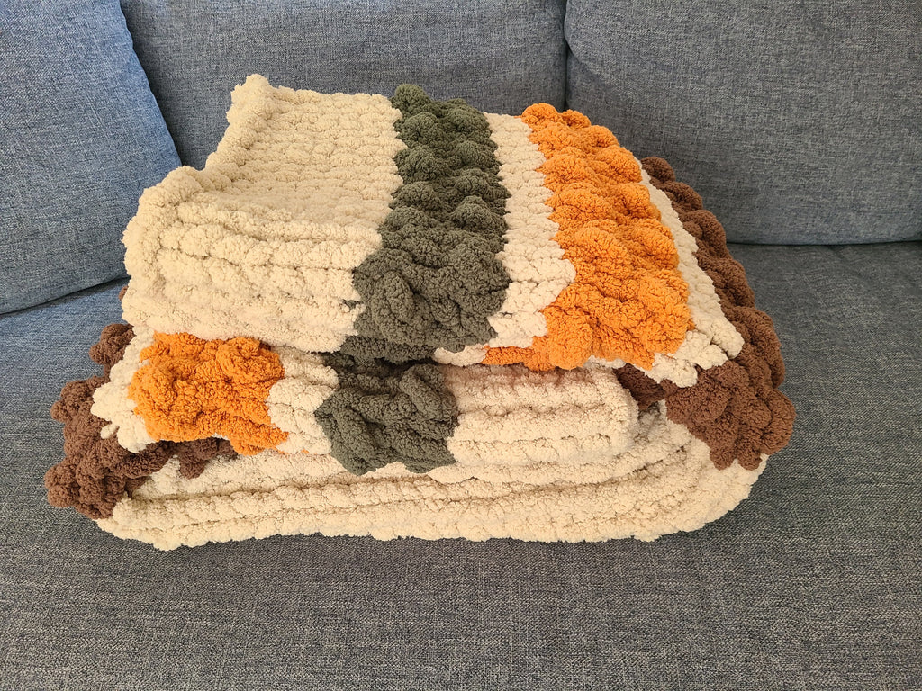 Woodland Ridge — olive, butterscotch, and taupe on oatmeal — folded on a gray sofa showing the bobble texture