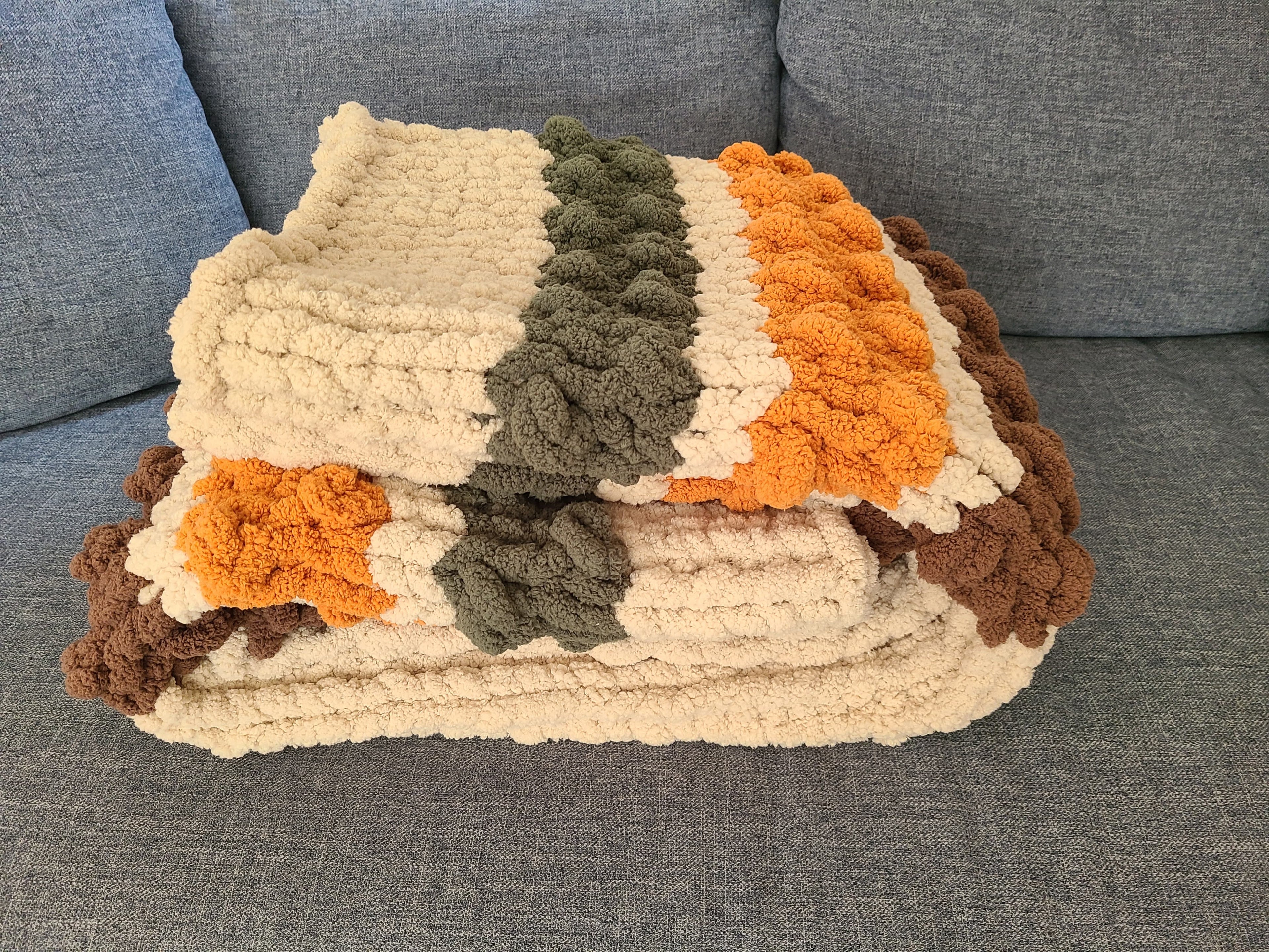 Woodland Ridge — olive, butterscotch, and taupe on oatmeal — folded on a gray sofa showing the bobble texture