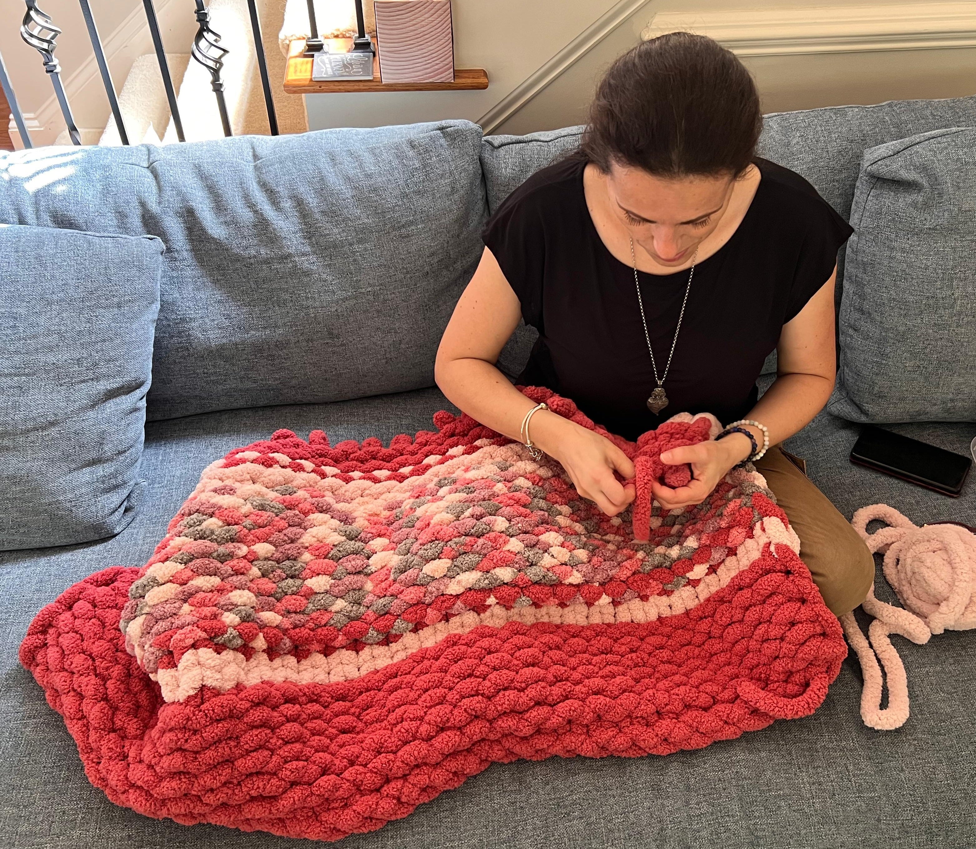 Sonia hand-knitting a chunky chenille blanket on her sofa